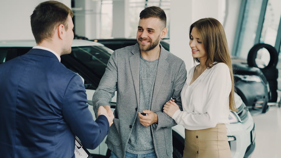 Happy couple finalizing car purchase with salesman in dealership showroom. Bright and welcoming environment
